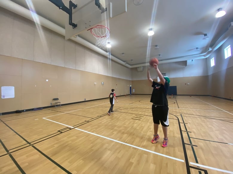 A kid throws a basketball at a hoop in a gymnasium. 